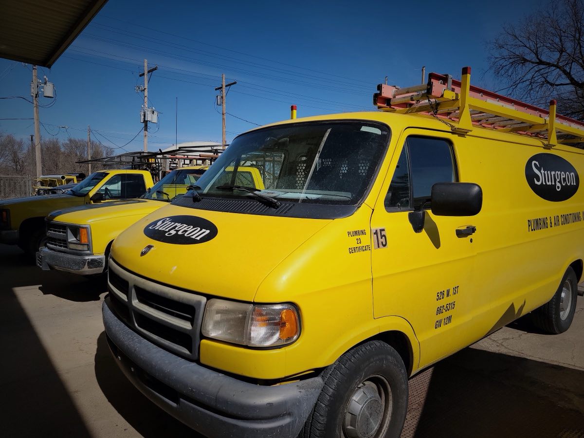 Fleet of bright yellow Sturgeon Plumbing and Air service vans and trucks parked at the shop in Hutchinson, Kansas